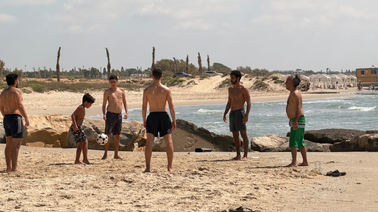 צעירים משחקים כדורגל על החוף של כפר הדייגים